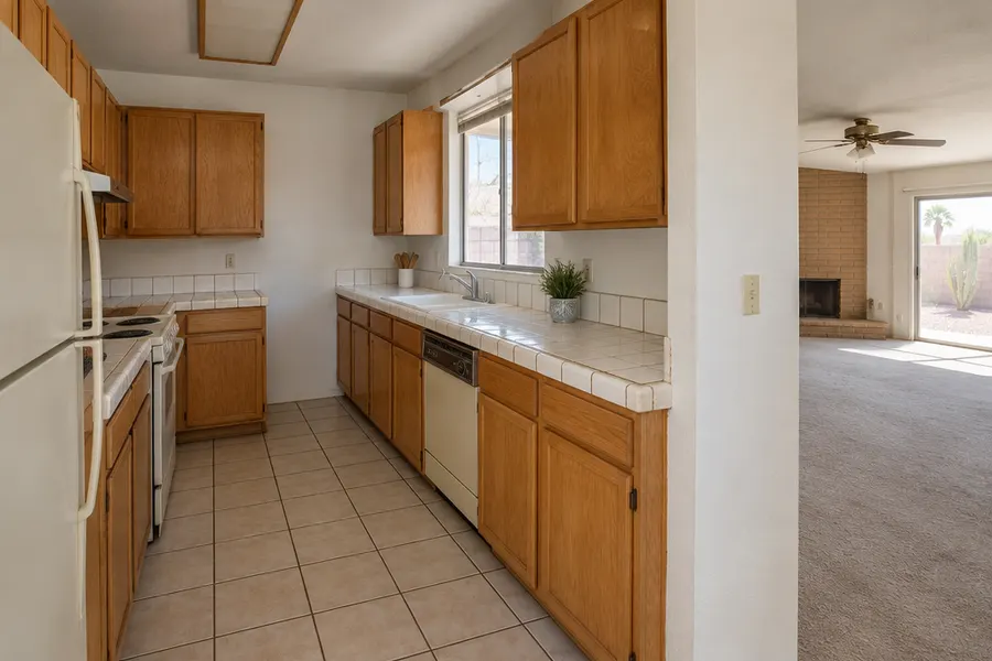 Dated Tempe kitchen before a remodel: honey oak cabinets, white tile countertops with stained grout, old almond appliances, wall closing it off from the living room